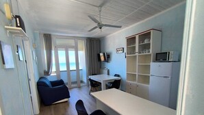 A compact room with a ceiling fan, a white table, a sofa, a TV, a microwave, and a refrigerator. - Termoli 10 meters from the sea (Termoli)