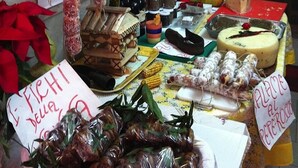 Ein Marktstand mit verschiedenen Lebensmitteln, darunter hängende Wurst, Gläser mit Marmelade und eine Käseauslage.