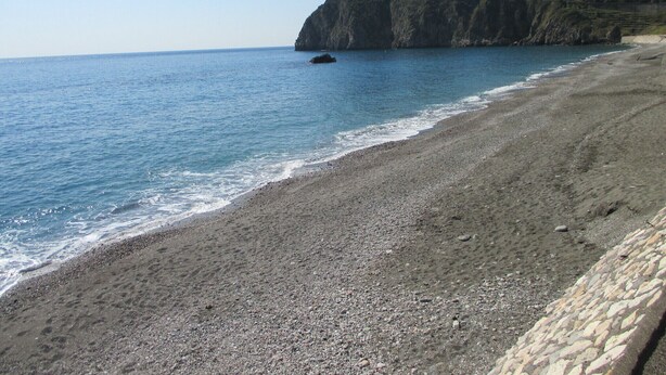 Ein felsiger Strand mit freiem Blick auf das Meer und einer Klippe mit Gebäuden darauf.