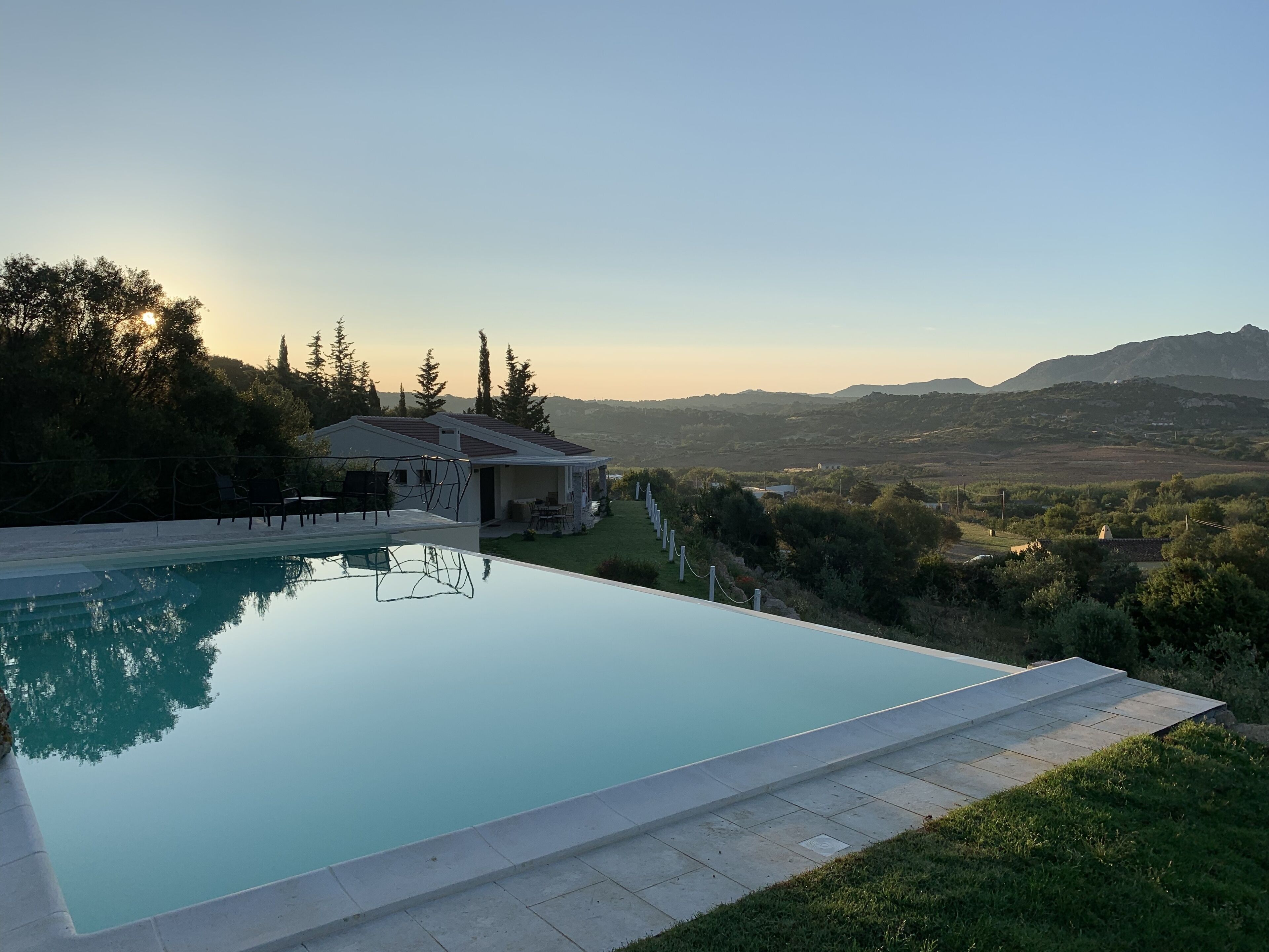 A modern house with a swimming pool, surrounded by greenery and mountains in the background.