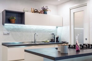 Una cocina moderna con encimera oscura, armarios blancos y un estante empotrado con objetos decorativos.