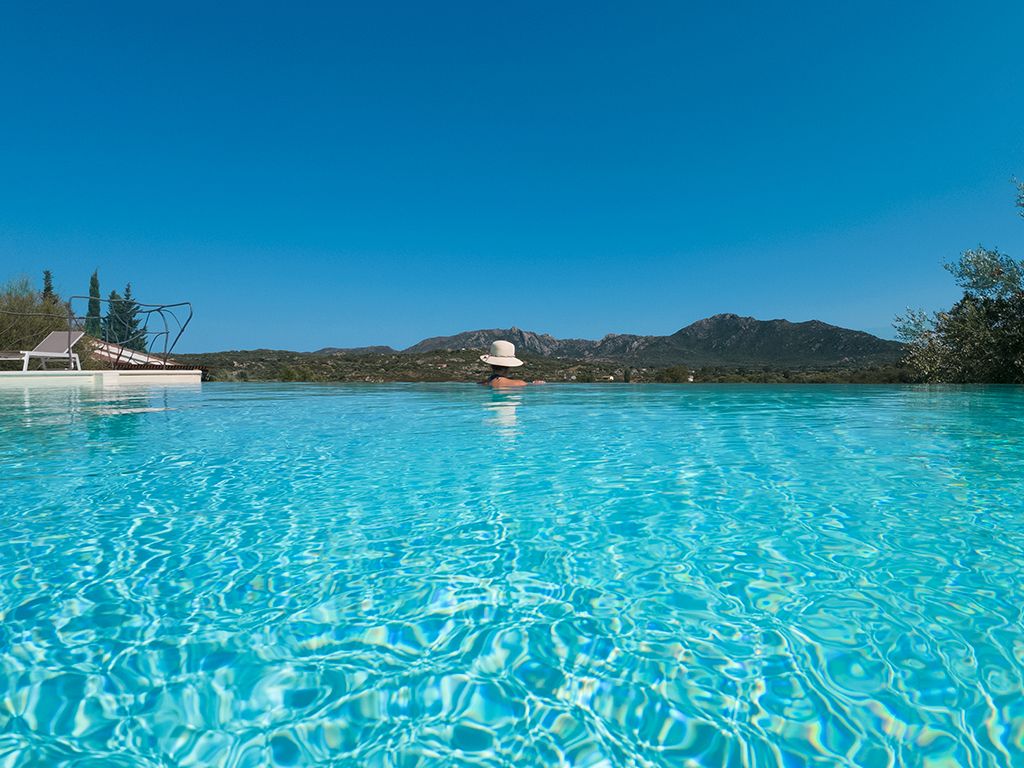 Une piscine d’eau cristalline, avec une chaîne de montagnes en arrière-plan et un bateau amarré sur la gauche.