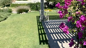 Eine Hollaube mit freiem Blick auf einen gepflegten Garten und ein entferntes Gebäude.