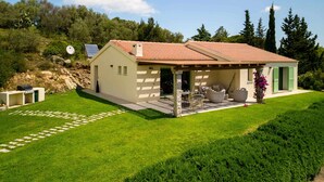 Ein eingeschossiges Haus mit Ziegeldach, einer überdachten Terrasse mit Gartenmöbeln und einem gepflegten Rasen.