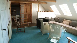 A cozy loft bedroom with a sloped ceiling, wooden beams, a large window, a sofa, a chair, and a ladder leading to an upper level. - North Sea vacation right before SPO; 6-8 people, large garden apartment skipper - (Tating)