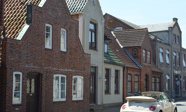 Une rangée de bâtiments traditionnels en briques, avec des fenêtres au design uniforme, et une voiture d’époque garée devant.