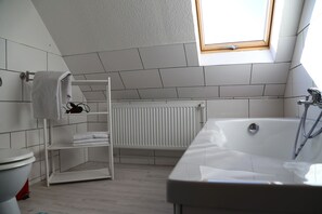 Une salle de bain moderne avec une lucarne, des carreaux blancs, une baignoire blanche et une étagère avec des serviettes.