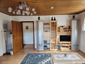 Ein Wohnzimmer mit Holzboden, einer Kandelaberleuchte, Einbauschränken, einem Flachbildfernseher und einem gemusterten Teppich.