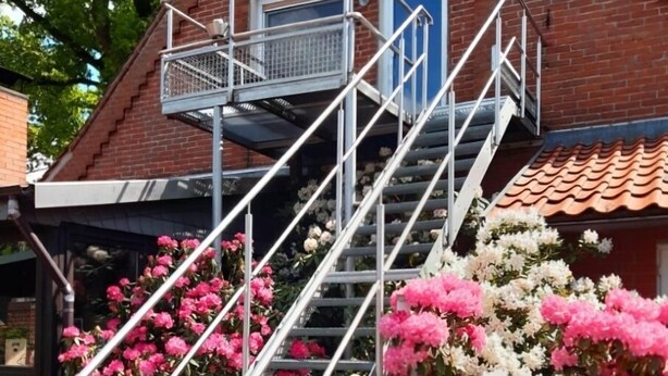 A brick building with a metal staircase leading to a blue door. - Apartment in quiet location (Frankenfeld-Bosse)