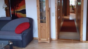 A modern living room with a grey sofa, a wooden cabinet, and a hallway leading to another room. - Apartment in quiet location (Frankenfeld-Bosse)