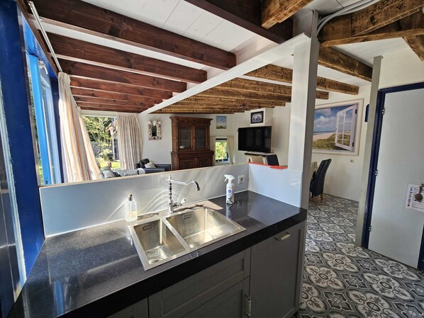 A modern kitchen with a black countertop, stainless steel sink, and wooden ceiling beams.