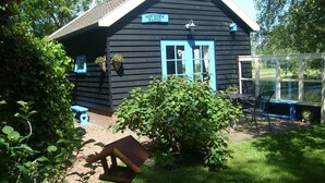 Une petite maison en bois noire, avec une porte et des fenêtres bleues, portant l’inscription « Hortensia Eiland ».