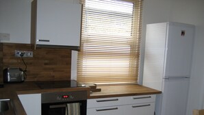 A compact kitchen with wooden cabinetry, a built-in oven, a toaster, and a refrigerator. - Beautiful 3 bedroom apartment in London (Tooting)