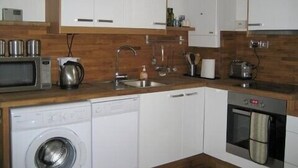 A compact kitchen with white cabinets, a microwave, a kettle, a sink, and a dishwasher. - Beautiful 3 bedroom apartment in London (Tooting)
