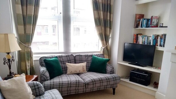 A living room with a plaid sofa, a television, and a bookshelf with books. - Beautiful 3 bedroom apartment in London (Tooting)