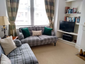 A living room with a plaid sofa, a television, and a bookshelf with books. - Beautiful 3 bedroom apartment in London (Tooting)