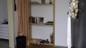 Um quarto com estante, um cesto de lixo preto, uma porta com cortina e um porta-toalhas fixado na parede.