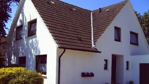 Uma casa branca de dois andares com telhado de telhas marrons, uma porta da frente e um pequeno alpendre.