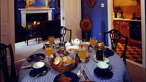 Een ontbijttafel gedekt met etenswaren, een kroonluchter en een blauwe wand met een open haard.