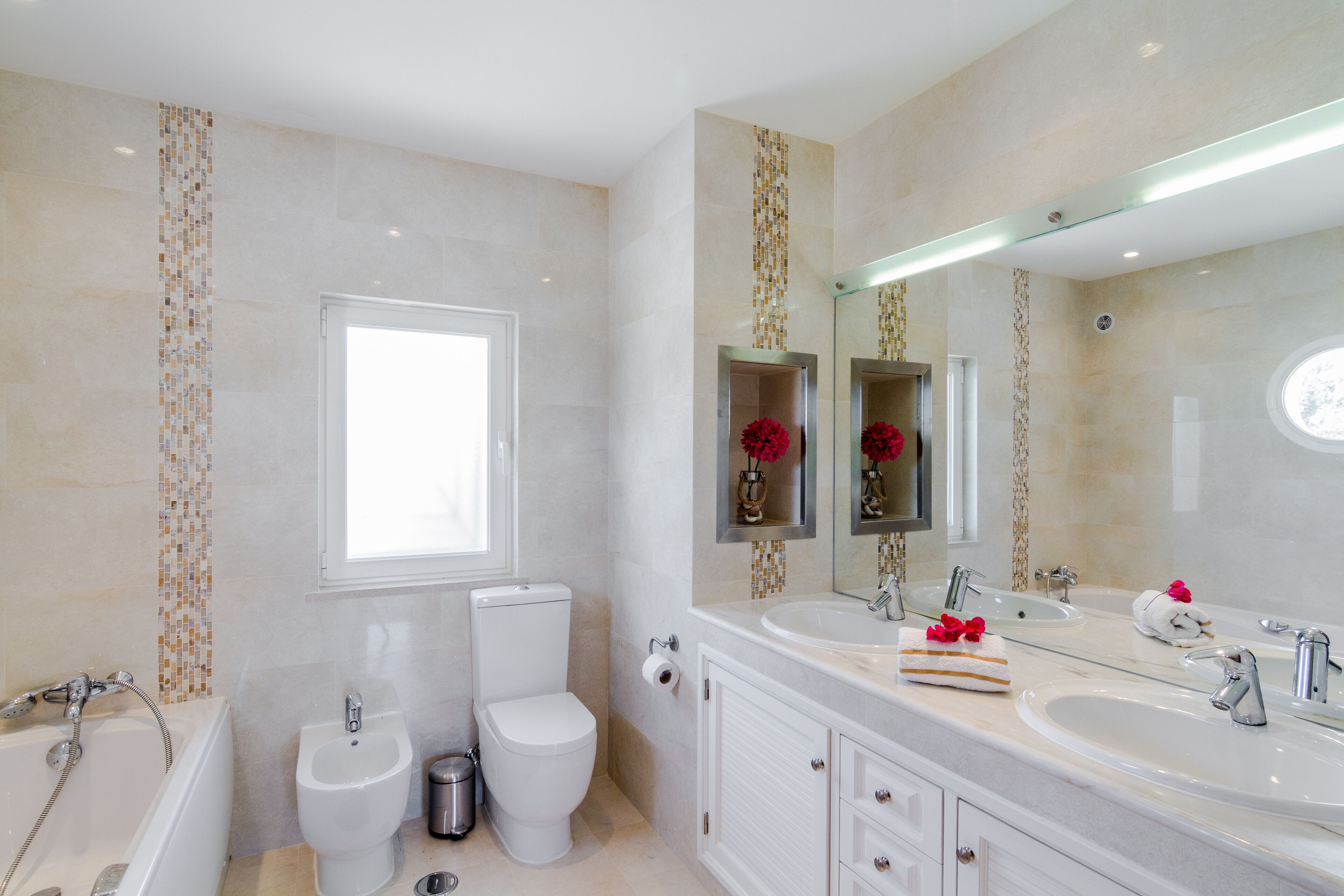 Une salle de bain moderne équipée d’une baignoire, de toilettes, d’un bidet et d’un meuble-lavabo à deux vasques.