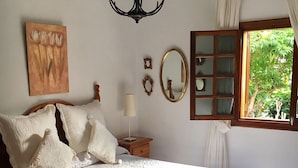 Een slaapkamer met een groot bed, een kroonluchter, een schilderij, een spiegel en een raam met gordijnen.
