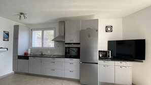 A modern kitchen with grey cabinets, a stainless steel refrigerator, a microwave, and a flat-screen TV.