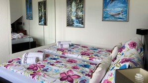 A hotel room with a bed, a large mirror, and two framed tropical paintings on the wall.