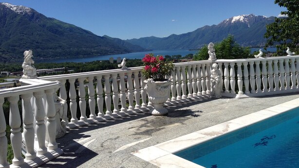 A poolside view with a balustrade, a statue, and a mountain backdrop.