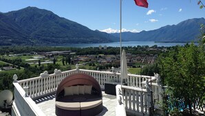 A balcony with a Swiss flag, overlooking a mountainous landscape and a lake.