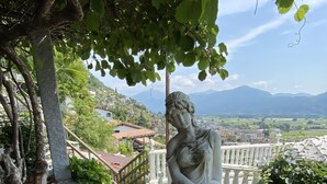 A statue of a woman holding a child, surrounded by greenery and a view of a town and mountains in the background.