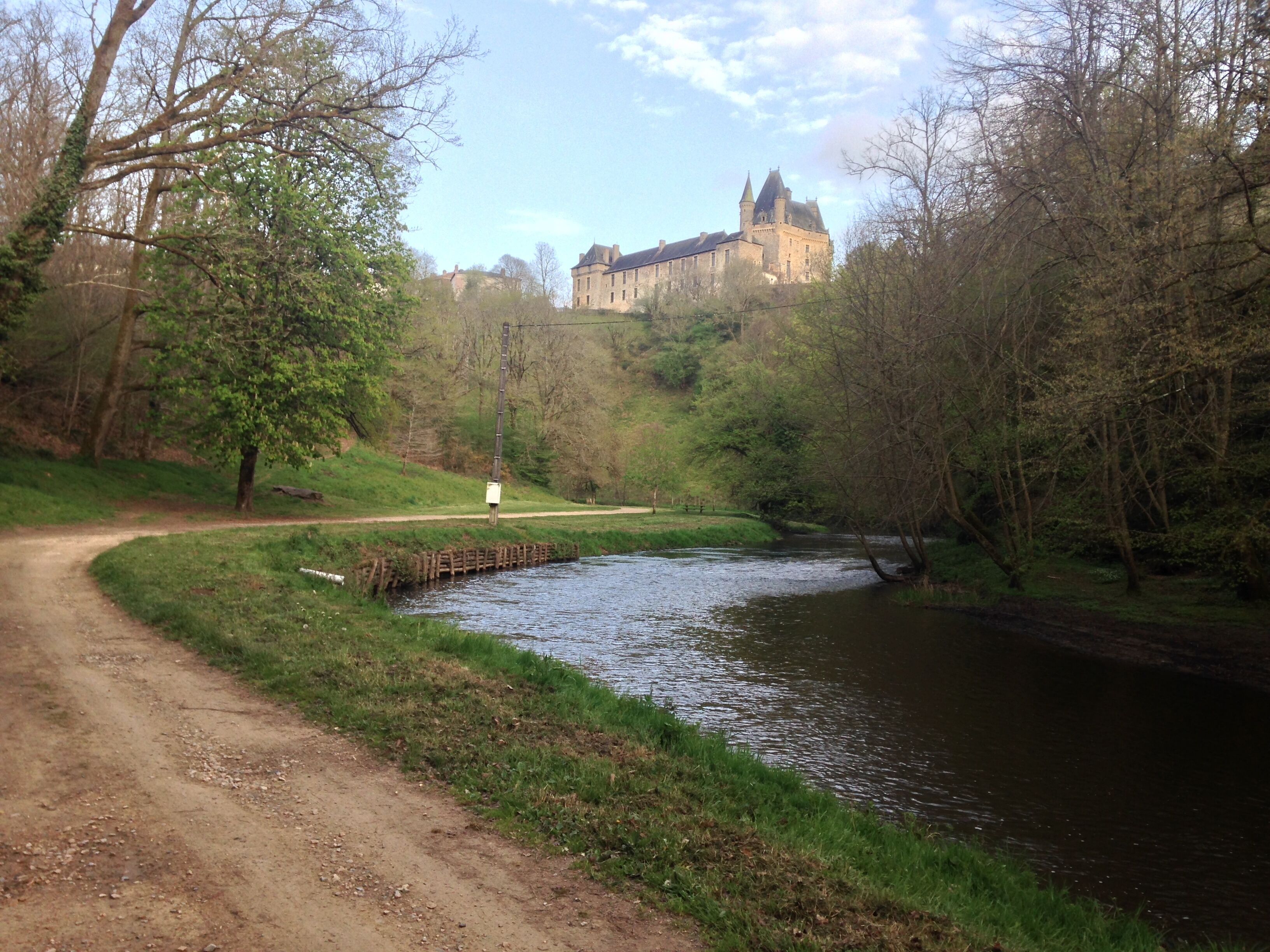 A river with a bridge, surrounded by trees and a castle in the background.