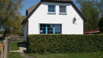 Une maison blanche avec un toit de chaume, une haie devant et un chemin de pierres menant à l’entrée.
