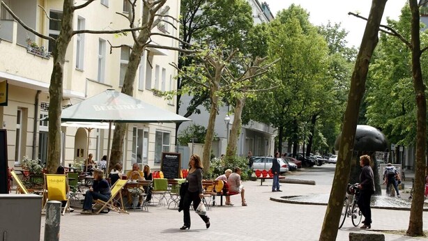 A street with outdoor seating, trees, and a cyclist.