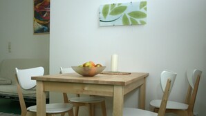 A dining area with a wooden table, white chairs, a bowl of fruit, and a candle.
