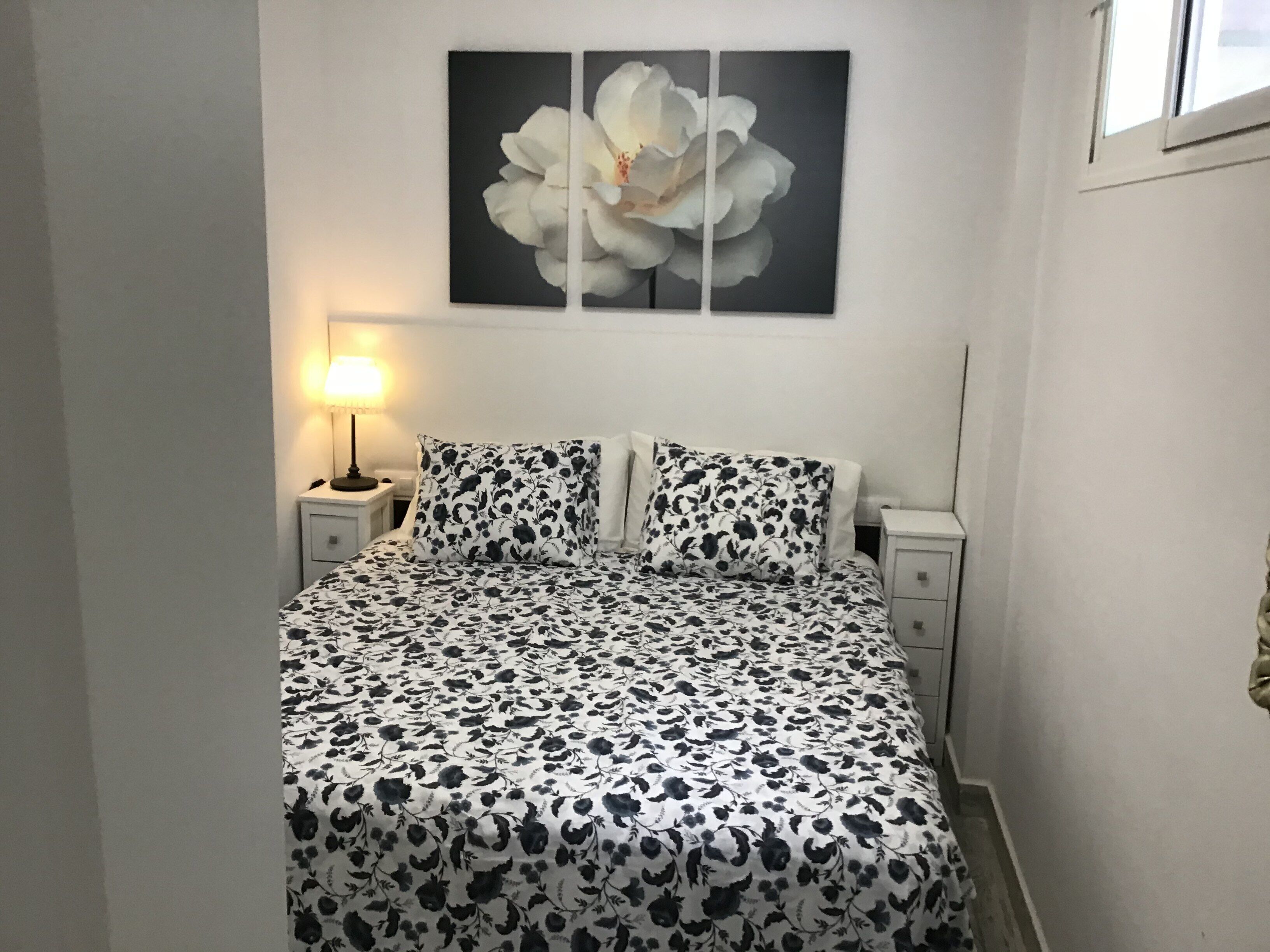 A bedroom with a bed, two nightstands, a lamp, and a large floral painting on the wall.