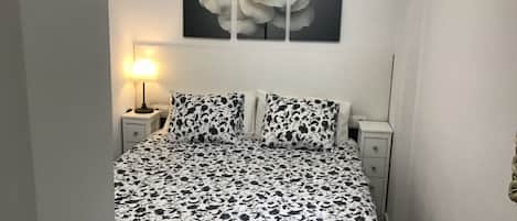 A bedroom with a bed, two nightstands, a lamp, and a large floral painting on the wall.