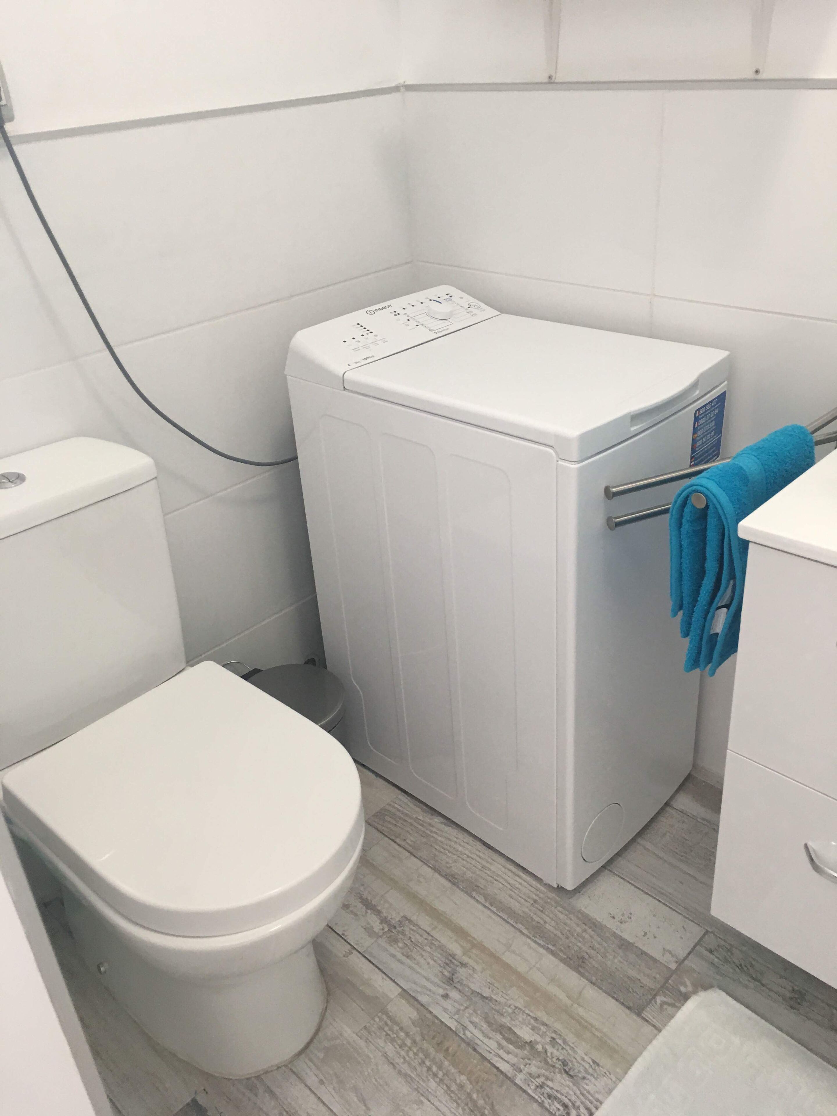 Et lille badeværelse med toilet, vaskemaskine og et skab.