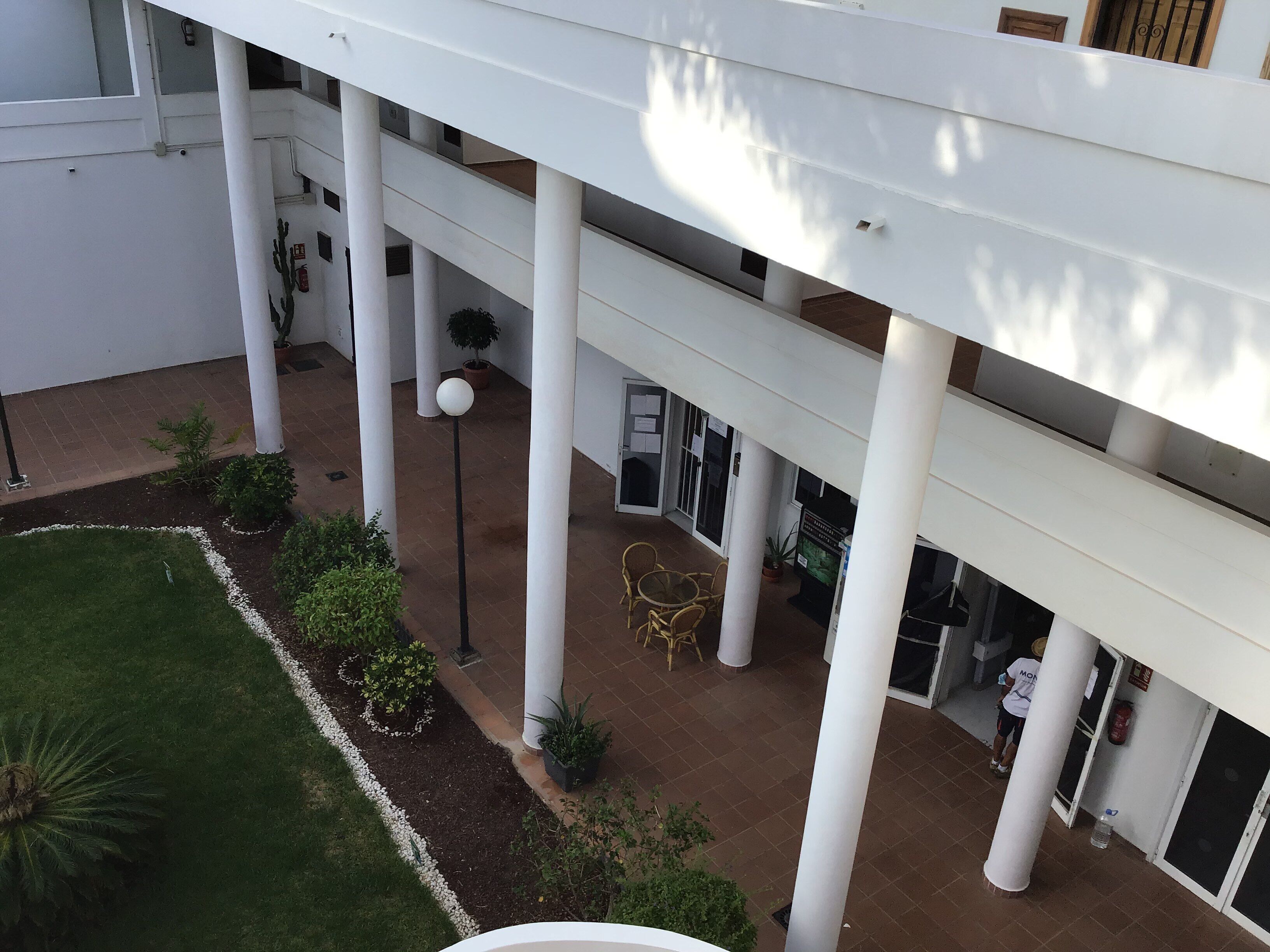 A multi-level building with white columns, outdoor seating, and a small garden area.