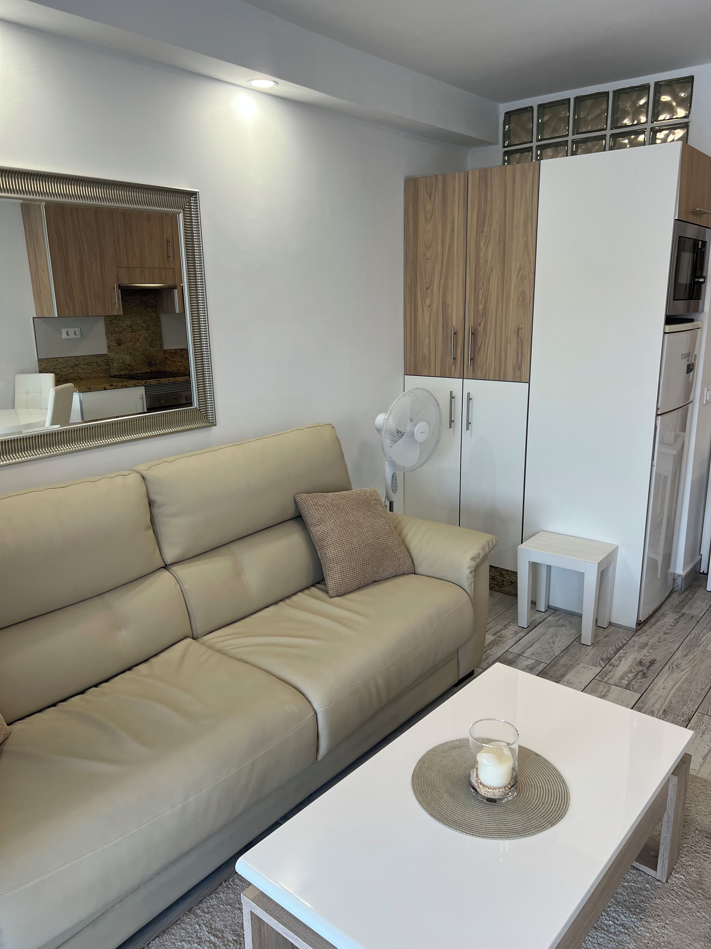 Un salon moderne avec un canapé beige, une table basse blanche et une petite table d’appoint blanche.