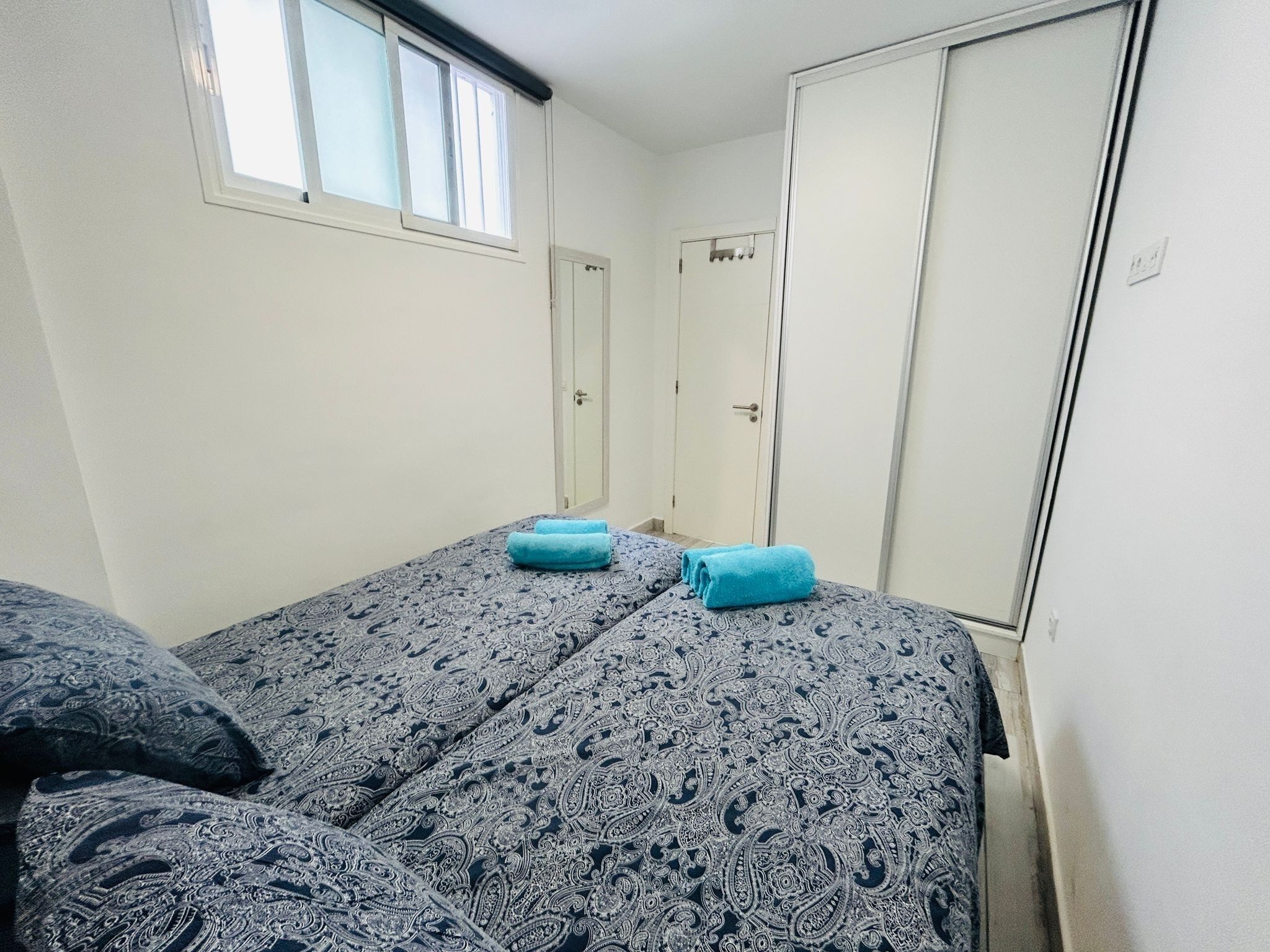 A small, single-room accommodation with two beds, a wardrobe, and a window.