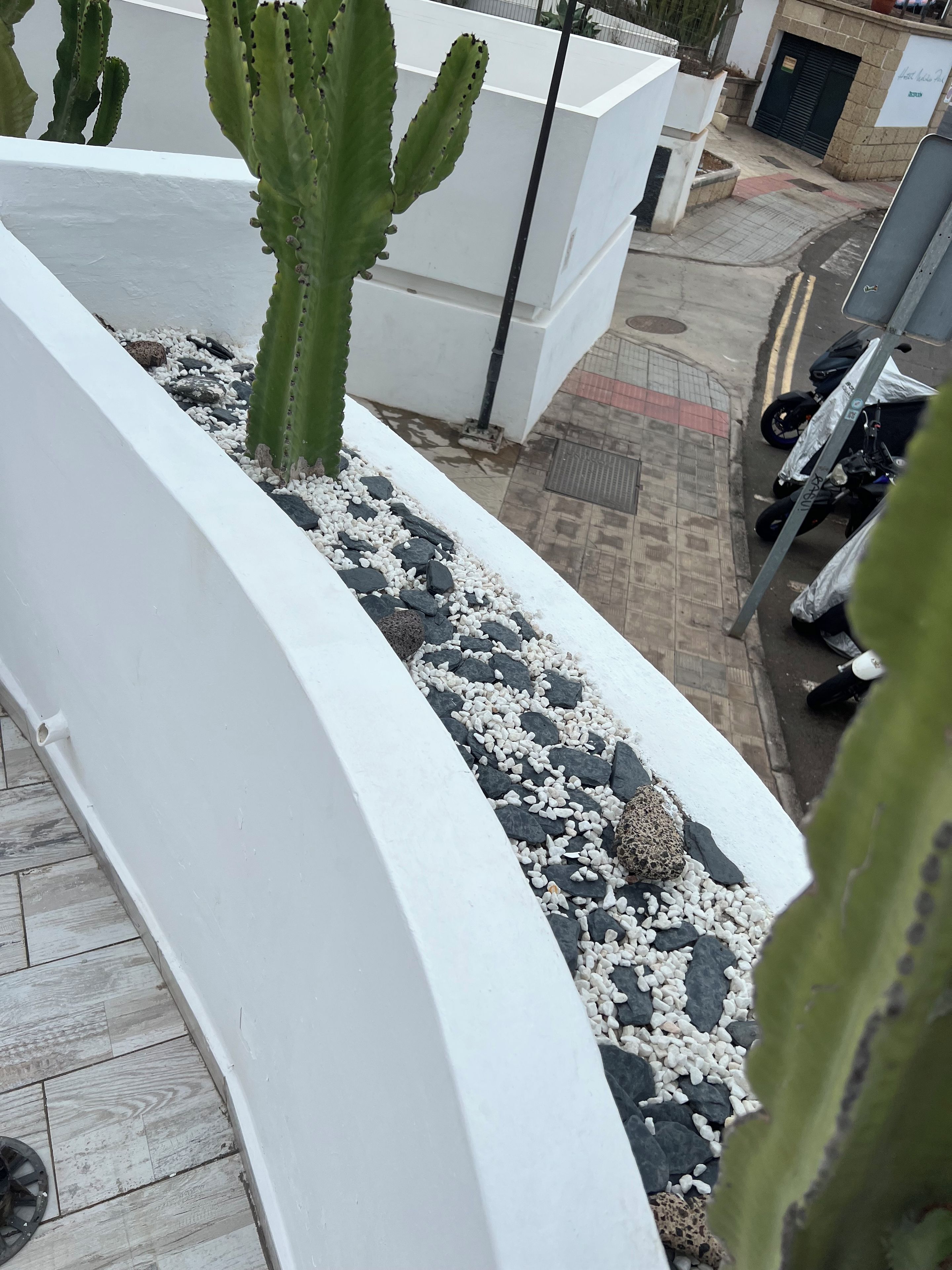 Un balcon avec une balustrade blanche, un cactus et un mélange de galets clairs et foncés.