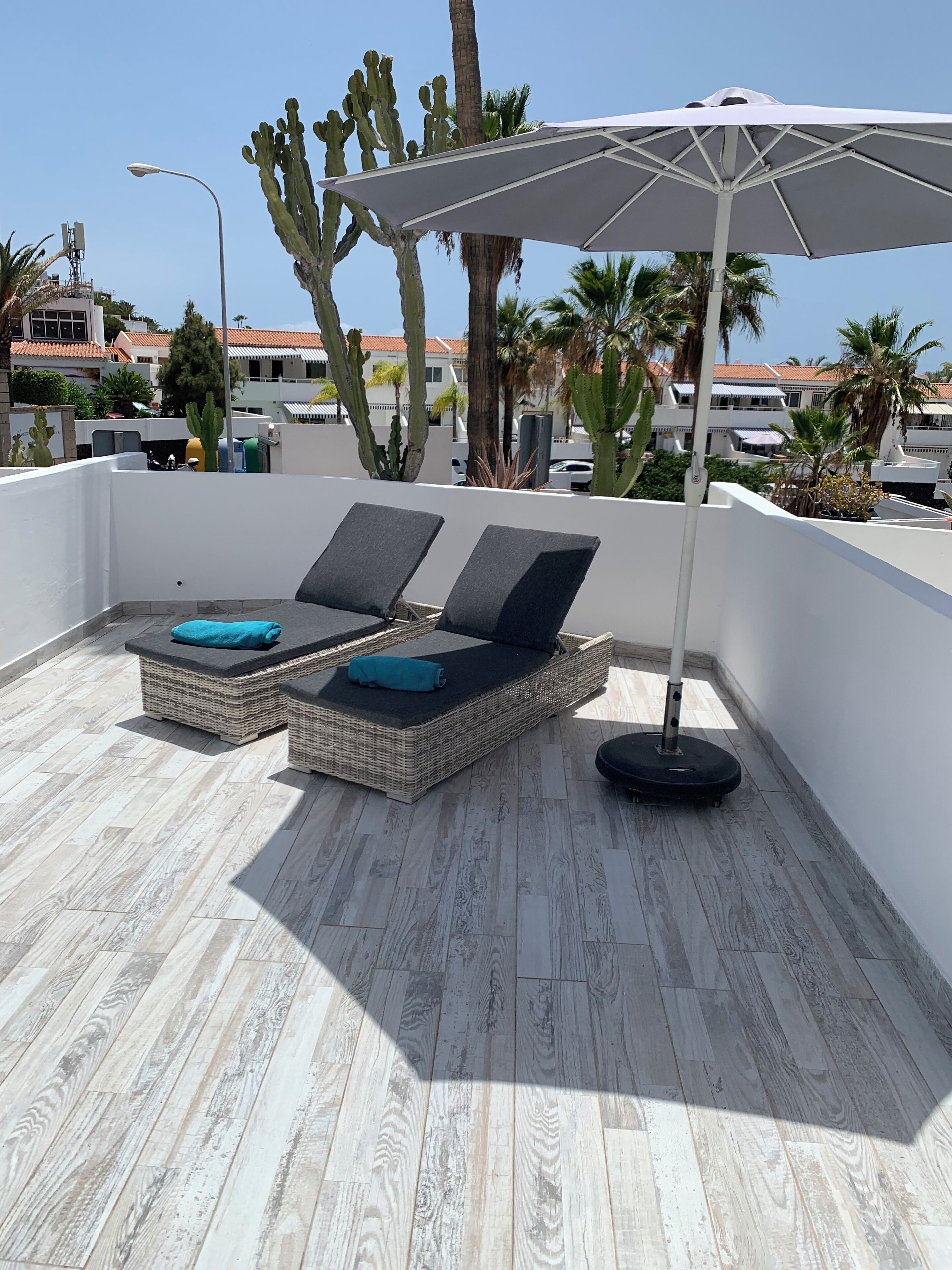 Una terraza en la azotea con dos sillones de mimbre, una sombrilla blanca y un cactus al fondo.