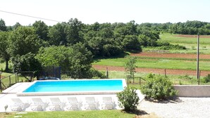 A swimming pool with lounge chairs, surrounded by a fence and trees, with fields in the background. - Vocation Home Ana In Kringa Istra, 8 Persons, 3bedrooms, 2 Bathrooms, with Pool (TINJAN)