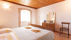 A bedroom with a wooden ceiling, a stone archway, a bed with a quilted bedspread, a wooden dresser, a chair, and a mirror on the wall. - Vocation Home Ana In Kringa Istra, 8 Persons, 3bedrooms, 2 Bathrooms, with Pool (TINJAN)