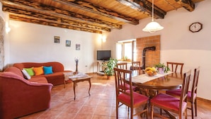 A cozy living room with a red sofa, wooden dining table, and chairs. There is a TV and a fireplace in the background. - Vocation Home Ana In Kringa Istra, 8 Persons, 3bedrooms, 2 Bathrooms, with Pool (TINJAN)