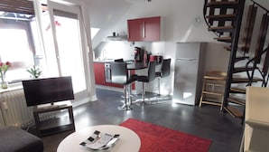 Un salon moderne avec un téléviseur à écran plat, une petite table sur laquelle est posé un magazine et un tapis rouge.
