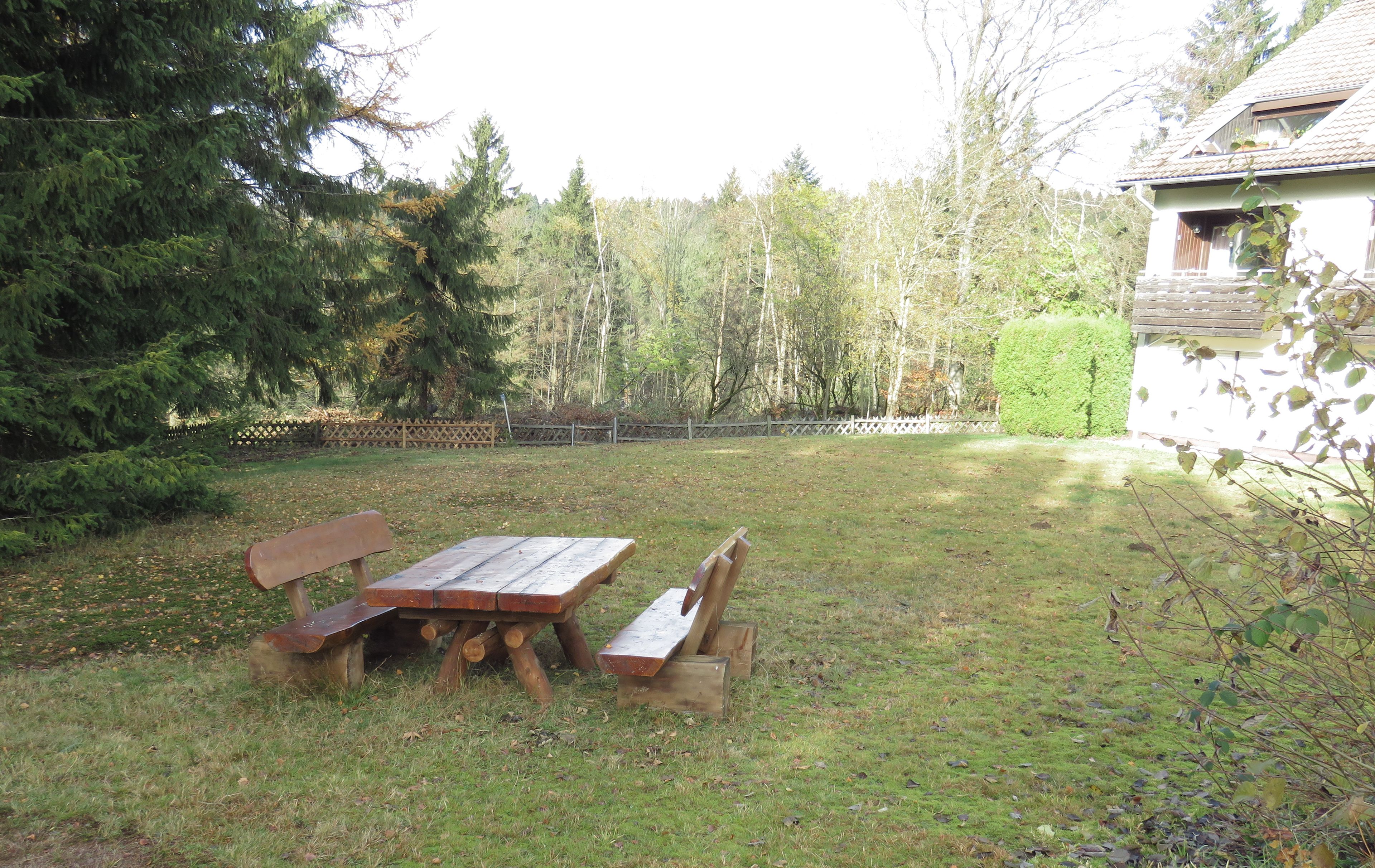 Une table de pique-nique et des bancs dans une cour arrière verdoyante, avec une maison en arrière-plan.