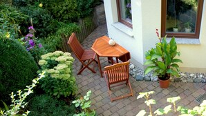 A patio with a wooden table and chairs, surrounded by lush greenery and potted plants. - Quiet holiday home, high quality, lovingly furnished (Dresden)