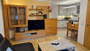 A modern living room with a flat-screen TV, wooden cabinets, a coffee table, and a dining area with chairs. - Quiet holiday home, high quality, lovingly furnished (Dresden)