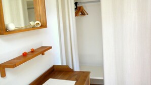 A wooden dresser with a mirror, a small shelf, and a white towel. There is a wooden hanger rack with clothes and a white curtain partially drawn. - Quiet holiday home, high quality, lovingly furnished (Dresden)